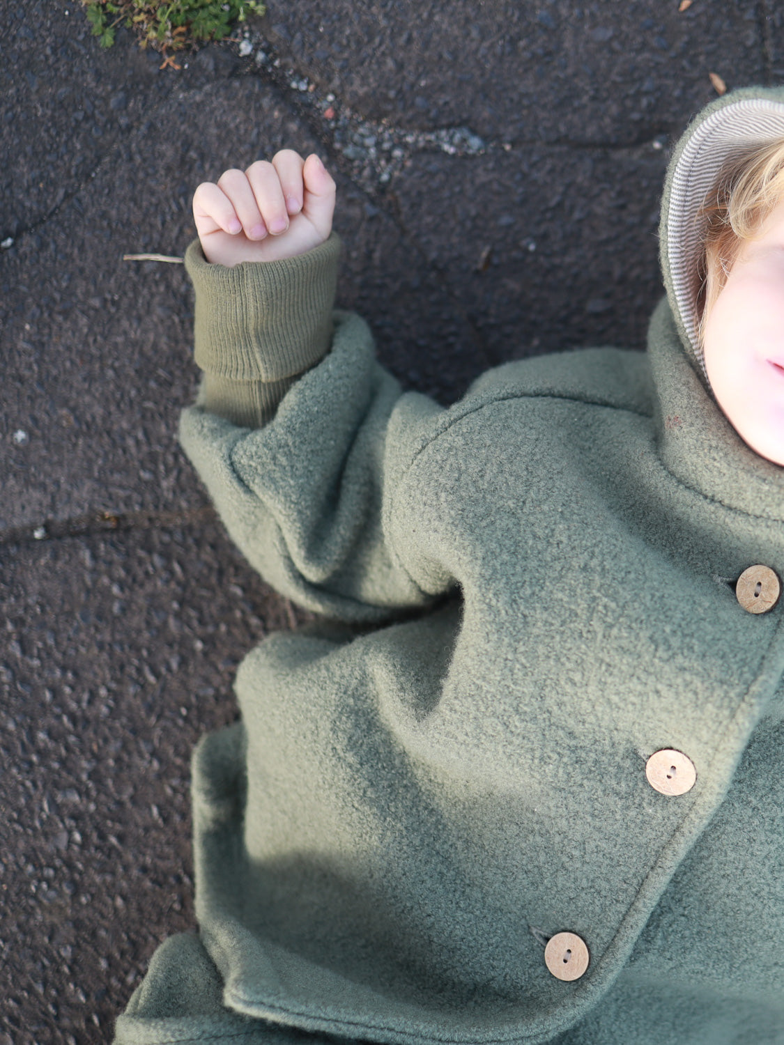 Kind liegt auf dem Boden, trägt die Wichteljacke Wollwalk - Pistazie von PETIT COCHON. Die Jacke bietet Bewegungsfreiheit und ist mit Bio-Jersey gefüttert, ideal für Herbst und Winter.  nachhaltige Kinderkleidung aus Wollwalk