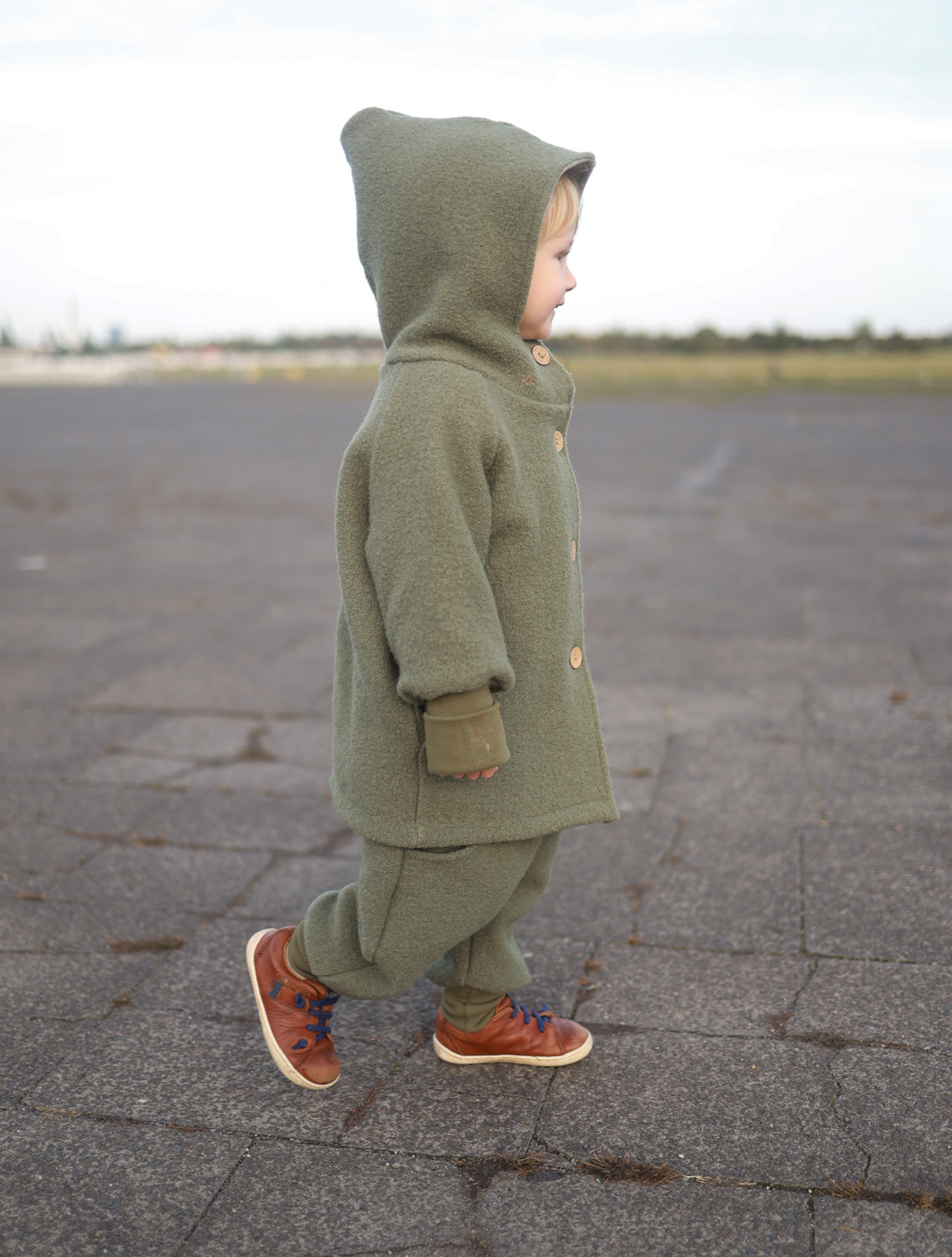Kind trägt die Wichteljacke Wollwalk - Pistazie mit Kapuze, aus Wollwalk und Bio-Jersey-Futter, ideal für Herbst bis Winter, bequemer Schnitt.