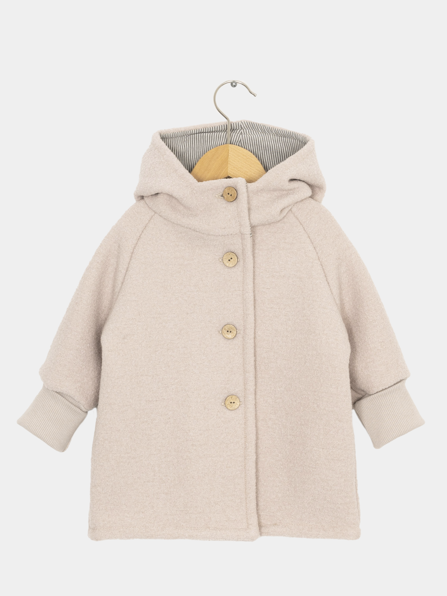 Wichteljacke Wollwalk - Sand: Kleinkind-Mantel aus weichem Wollwalk, mit Kapuze und gestreiftem Futter, gerippten Bündchen, und vier Holzknöpfen, auf einem Holzkleiderbügel vor weißem Hintergrund.