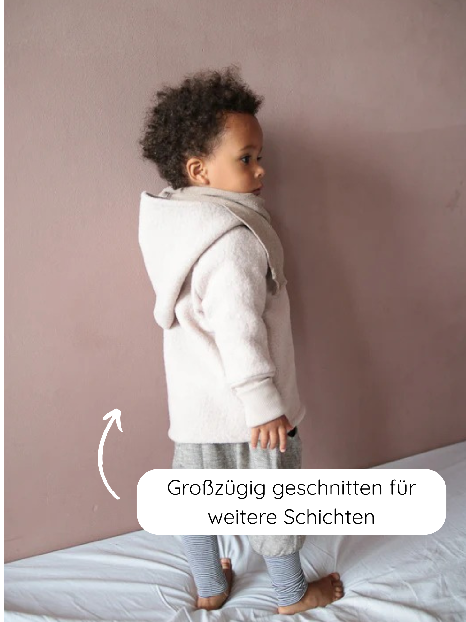 Ein Kleinkind trägt die Wichteljacke Wollwalk - Sand, großzügig geschnitten für mehrschichtiges Tragen. Die Jacke bietet Bewegungsfreiheit und ist mit Bio-Jersey gefüttert, ideal für kältere Jahreszeiten.