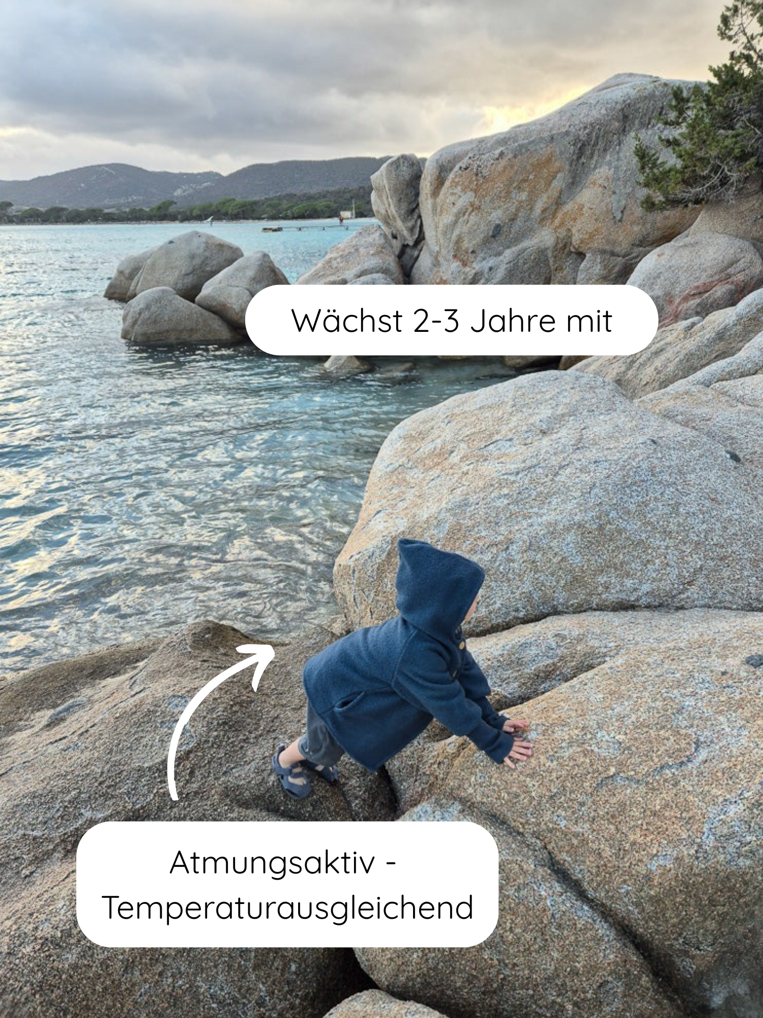 Wichteljacke Wollwalk - Marine: Ein Kleinkind klettert über große Küstenfelsen, trägt eine blaue, atmungsaktive Wollwalk-Jacke mit mitwachsendem Design, ideal für Herbst, Winter und Frühling.