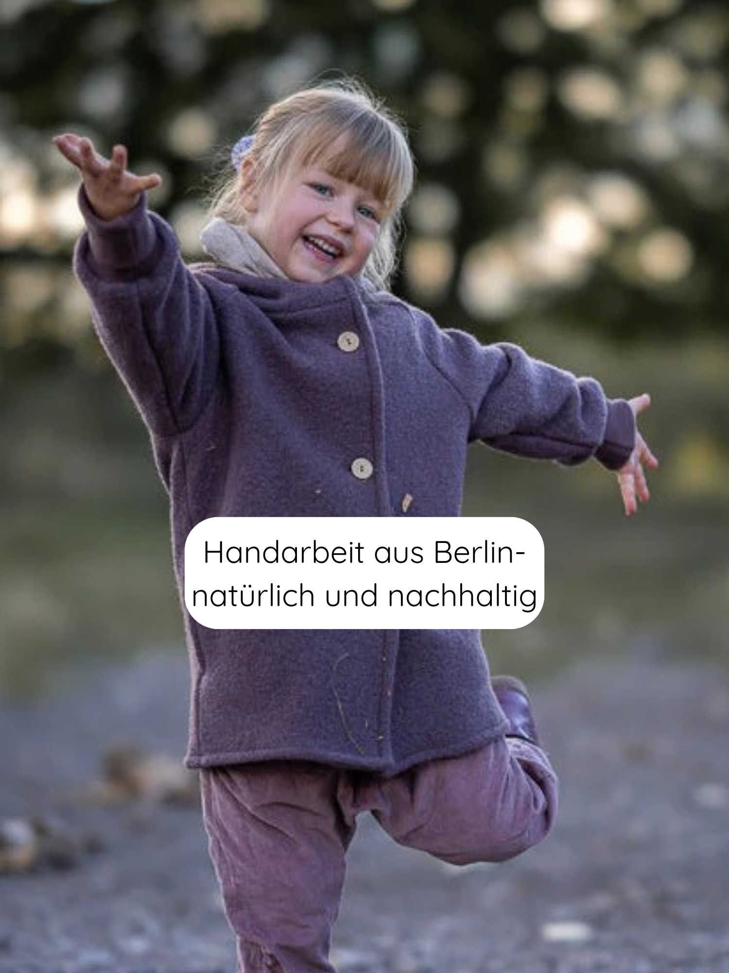 Ein Kind in Wichteljacke Wollwalk - Malve mit Holzknöpfen und krempelbaren Bündchen, lächelt mit ausgestreckten Armen auf einem Weg. Handarbeit aus Berlin, nachhaltig gefertigt.