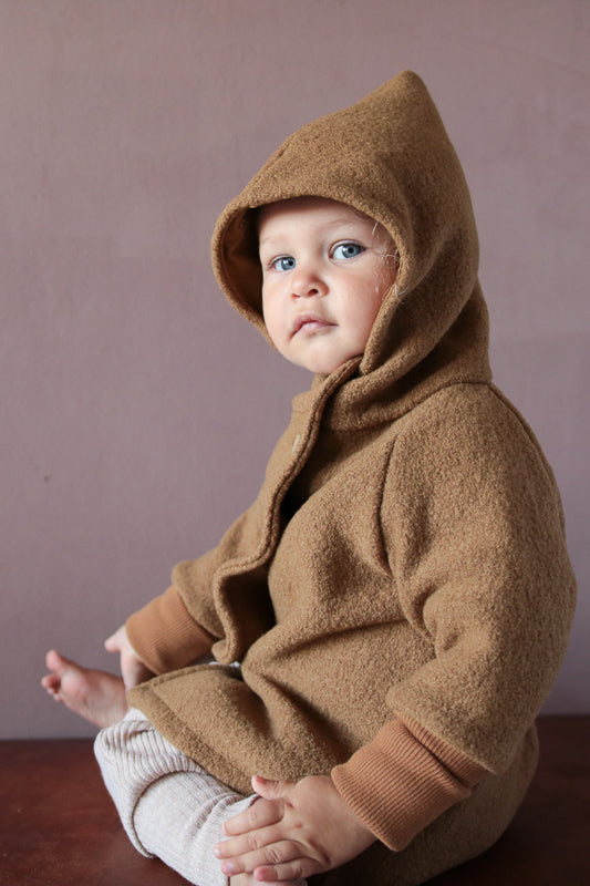 Ein Kleinkind trägt die Wichteljacke Wollwalk - Kamel, eine vielseitige, temperaturregulierende Jacke aus hochwertigem Wollwalk mit Bio-Baumwoll-Jersey-Futter von PETIT COCHON.