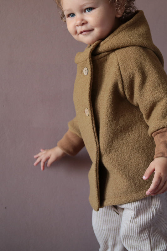 Kind trägt Wichteljacke Wollwalk - Kamel mit Bio-Jersey-Futter. Die Jacke bietet Bewegungsfreiheit und Temperaturregulierung, ideal für Herbst, Frühling und Winter. Krempelbare Bündchen für längere Nutzung. nachhaltige Kinderkleidung aus Wollwalk