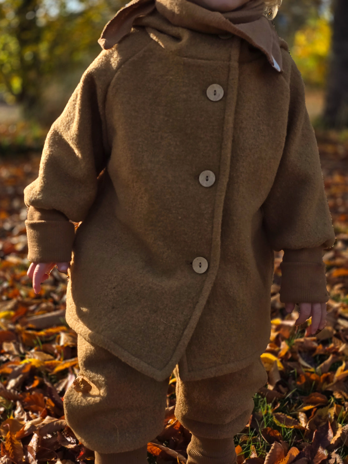 Kind trägt Wichteljacke Wollwalk - Kamel mit weißen Knöpfen, ideal für Herbst/Winter. Unisex-Design, krempelbare Bündchen, bietet Bewegungsfreiheit und Temperaturregulierung. Hochwertig verarbeitet aus zertifiziertem, italienischem Wollwalk.