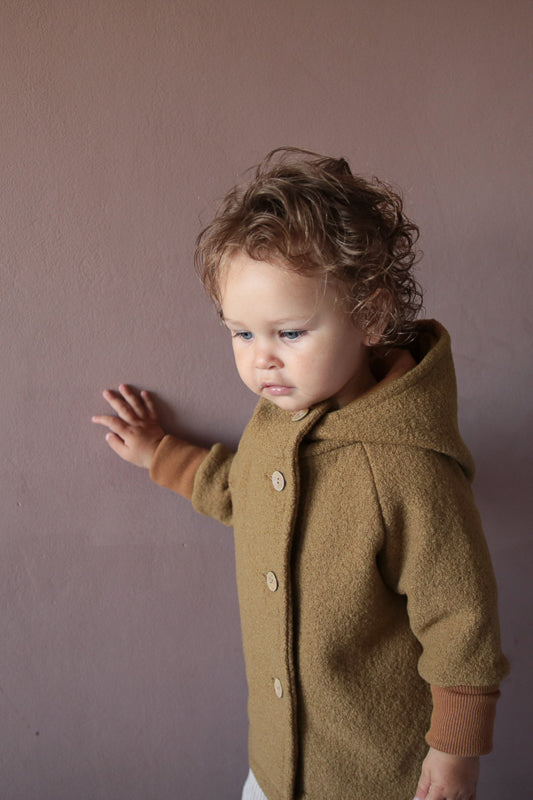 Ein Kind trägt die Wichteljacke Wollwalk - Kamel, eine hochwertige Wolljacke mit Bio-Jersey-Futter von PETIT COCHON, die Bewegungsfreiheit und temperaturregulierende Eigenschaften bietet. nachhaltige Kinderkleidung aus Wollwalk