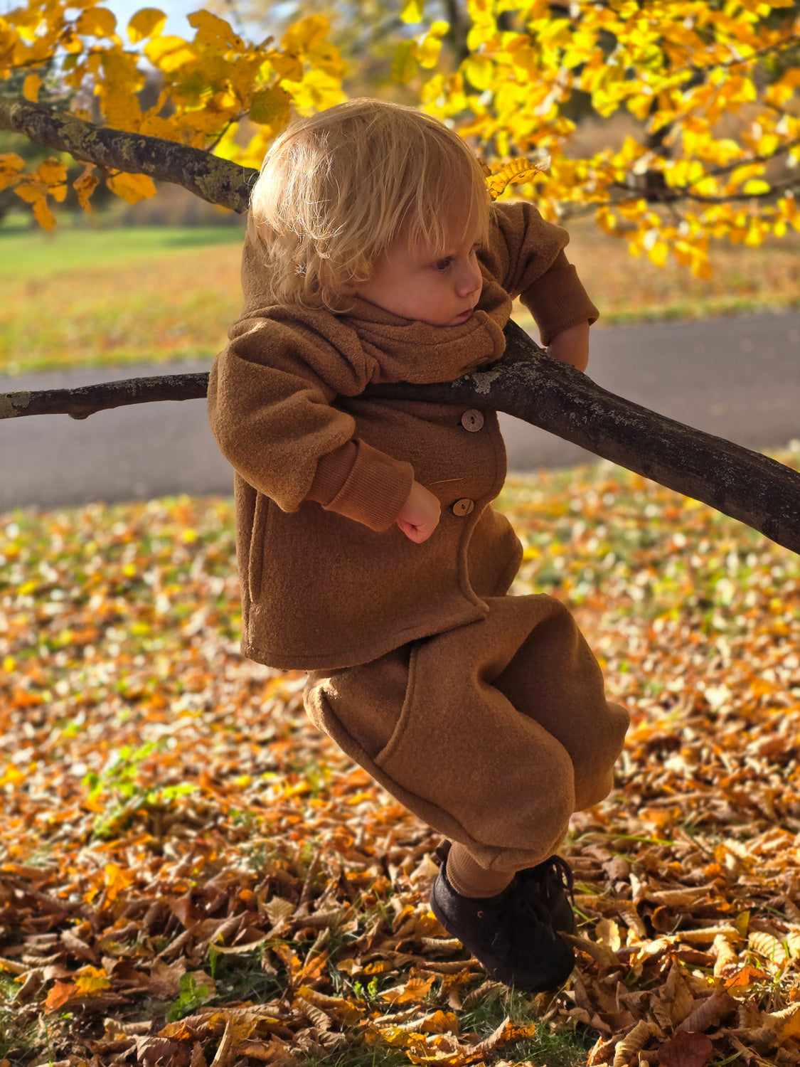 Kind klettert auf einem Baum, trägt die Wichteljacke Wollwalk - Kamel von PETIT COCHON, die durch Bewegungsfreiheit und temperaturregulierende Eigenschaften für Komfort sorgt. Unisex-Design für Geschwister nutzbar.