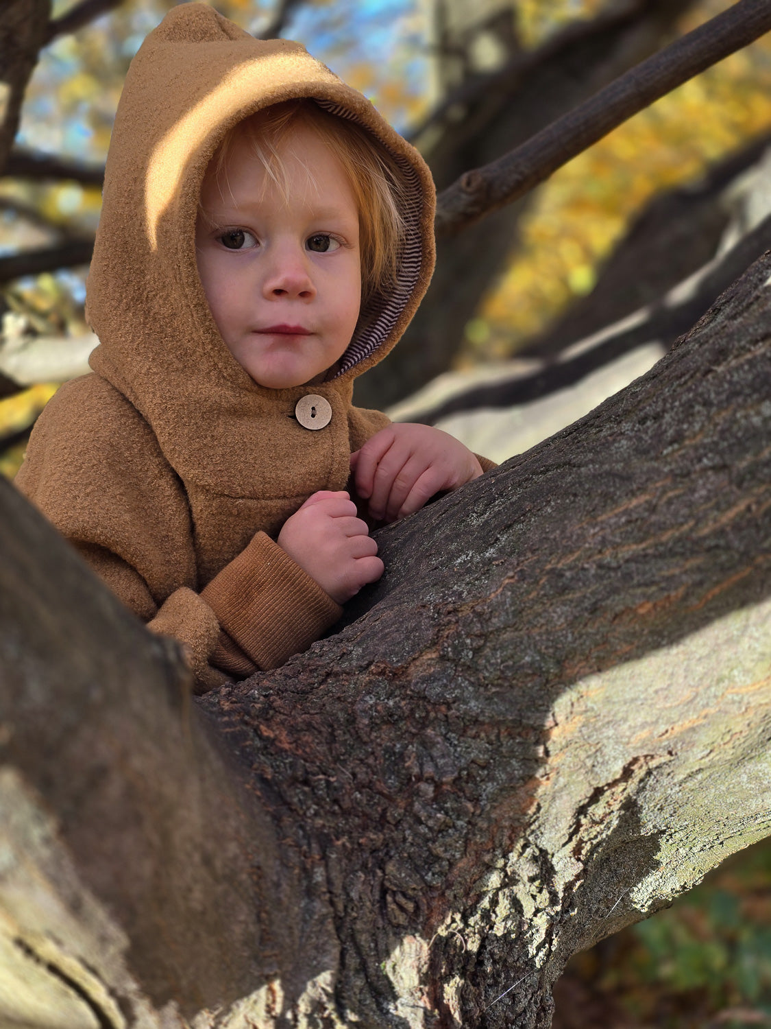 Ein Kind trägt die Wichteljacke Wollwalk - Kamel, eine warme Wollwalk-Jacke mit Kapuze und krempelbaren Bündchen, ideal für Herbst und Winter, bietet Bewegungsfreiheit und Temperaturregulierung.
