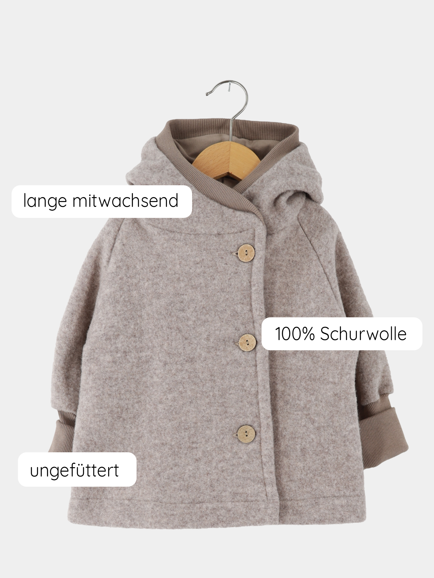Wichteljacke Merino Wollfleece - Hafer: Eine leichte, ungefütterte Kinderjacke aus 100% Schurwolle mit Kapuze, drei Holzknöpfen und wachsender Passform, hängend an einem Holzkleiderbügel.
