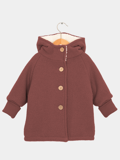 Teddy-Wichteljacke Wollwalk - Ziegel: Kinderjacke mit spitzer Kapuze, vier Holzknöpfen, weichem Teddyfutter, gerippten Bündchen und breitem Schnitt aus zertifiziertem Wollwalk, ideal für kalte Tage.