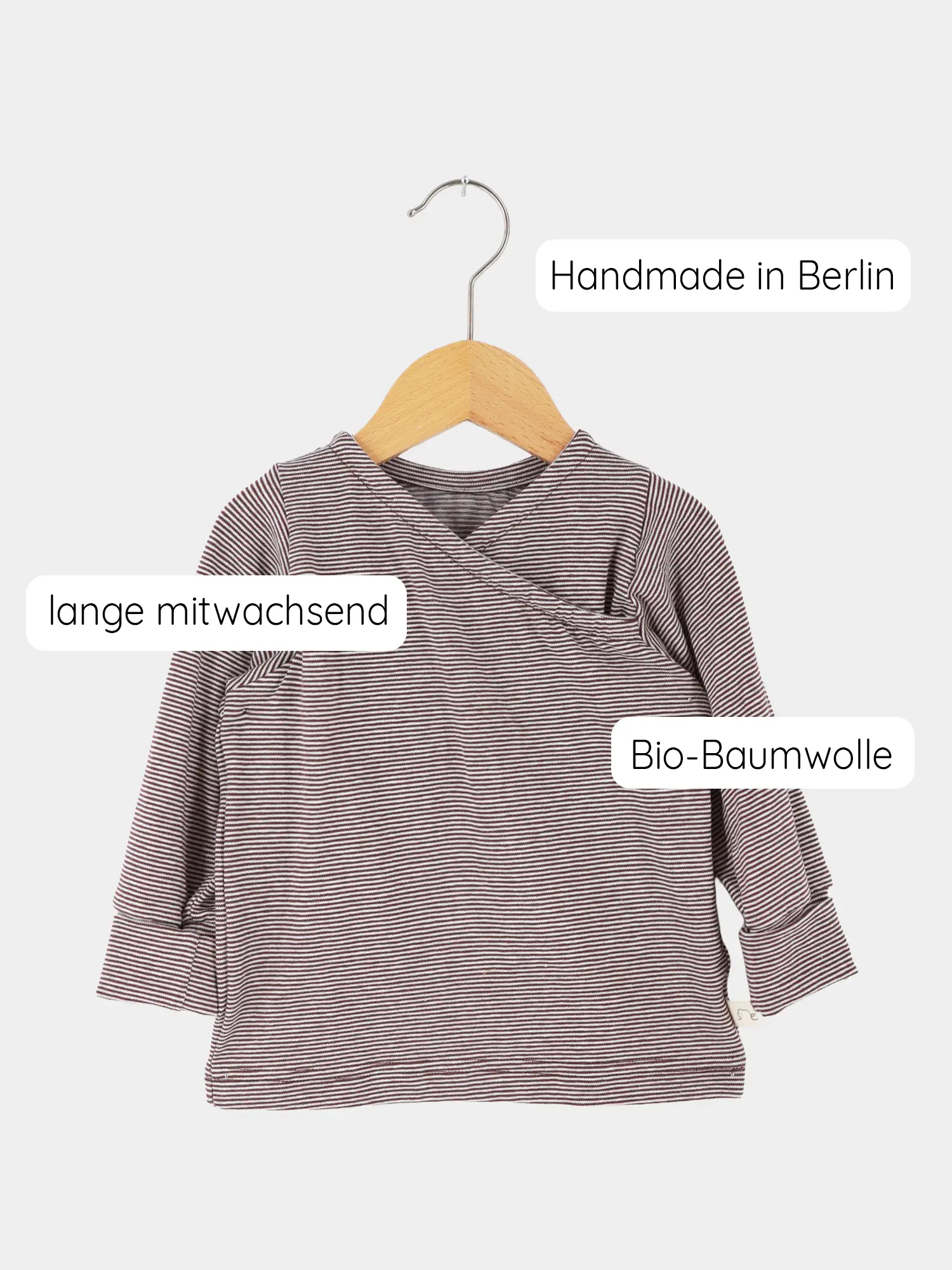 Wickelshirt aus Bio-Baumwolle - Ringel Schoko, langärmelig, auf Holzkleiderbügel. Zeigt dezentes Ringelmuster in Rotbraun und Off-White. Handgemacht in Berlin, mitwachsend, aus weichem, elastischem Bio-Stoff.