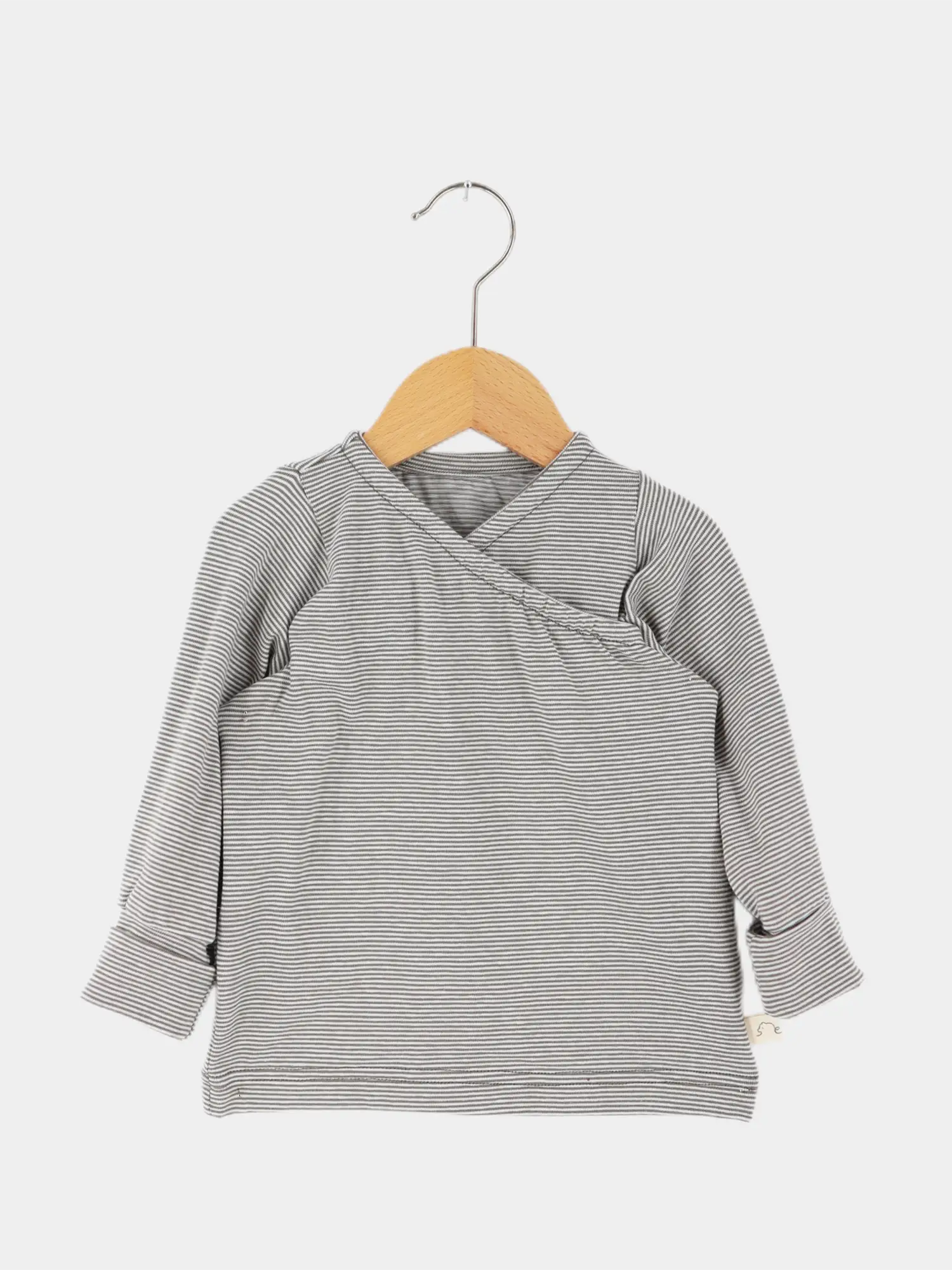 Wickelshirt aus Bio-Baumwolle - Ringel Maus: Langarmshirt für Babys mit Wickelschnitt, feine graue und weiße Streifen, leichtes Material, auf Holzkleiderbügel vor neutralem Hintergrund.
