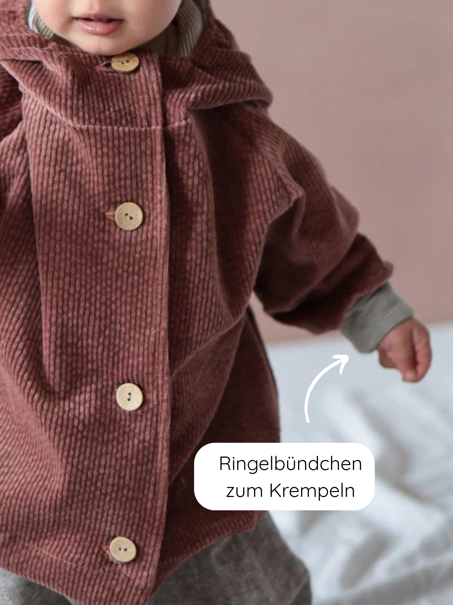 Kleines Kind in Wichteljacke Breitcord Stretch-Rosenholz mit runden Holzknöpfen. Ein Pfeil zeigt auf das krempelbare Ringelbündchen, das verstellbare Ärmel ermöglicht.