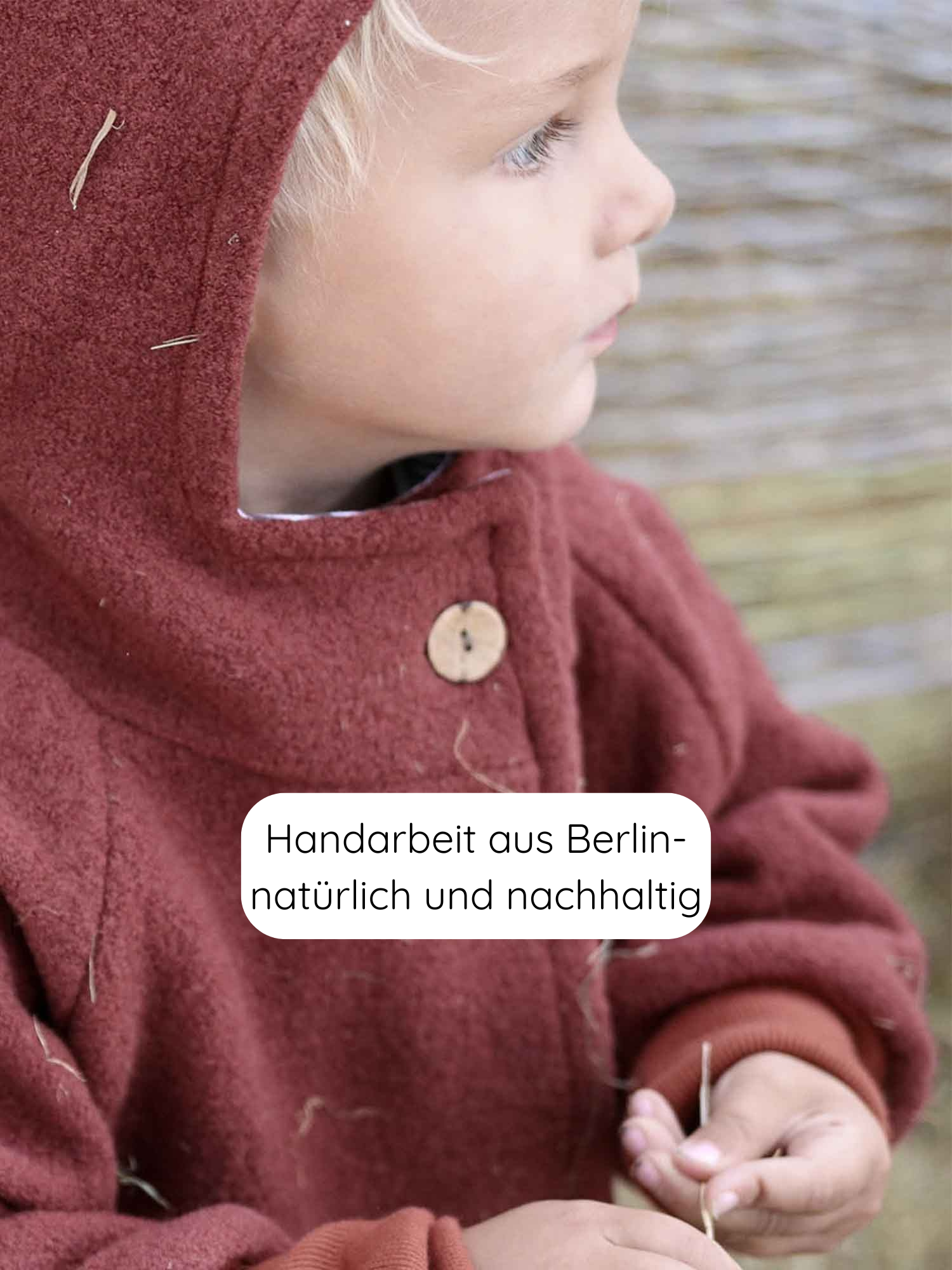 Kleinkind im Profil trägt Wichteljacke Wollwalk - Ziegel mit Holzknopf, hält Strohhalme. Handgefertigt in Berlin, nachhaltig, ideal für Herbst bis Frühling, mit Bio-Jersey-Futter, wachstumsfreundlich und vielseitig.