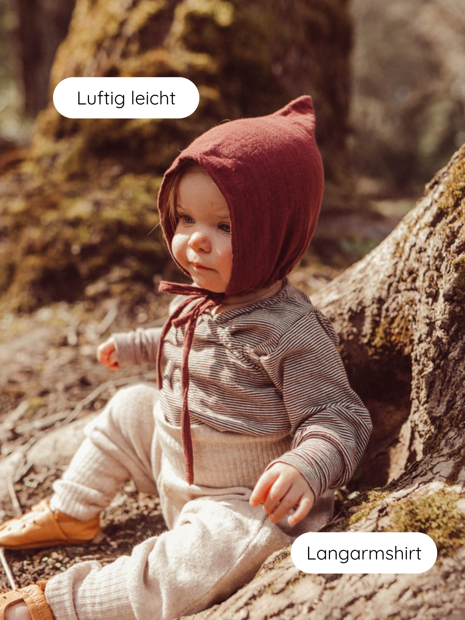 Kleinkind in Wickelshirt aus Bio-Baumwolle - Ringel Schoko sitzt an einem Baumstamm. Das Langarmshirt ist gestreift, kombiniert mit einer weichen Hose und spitzer Haube. Ideal für Neugeborene.