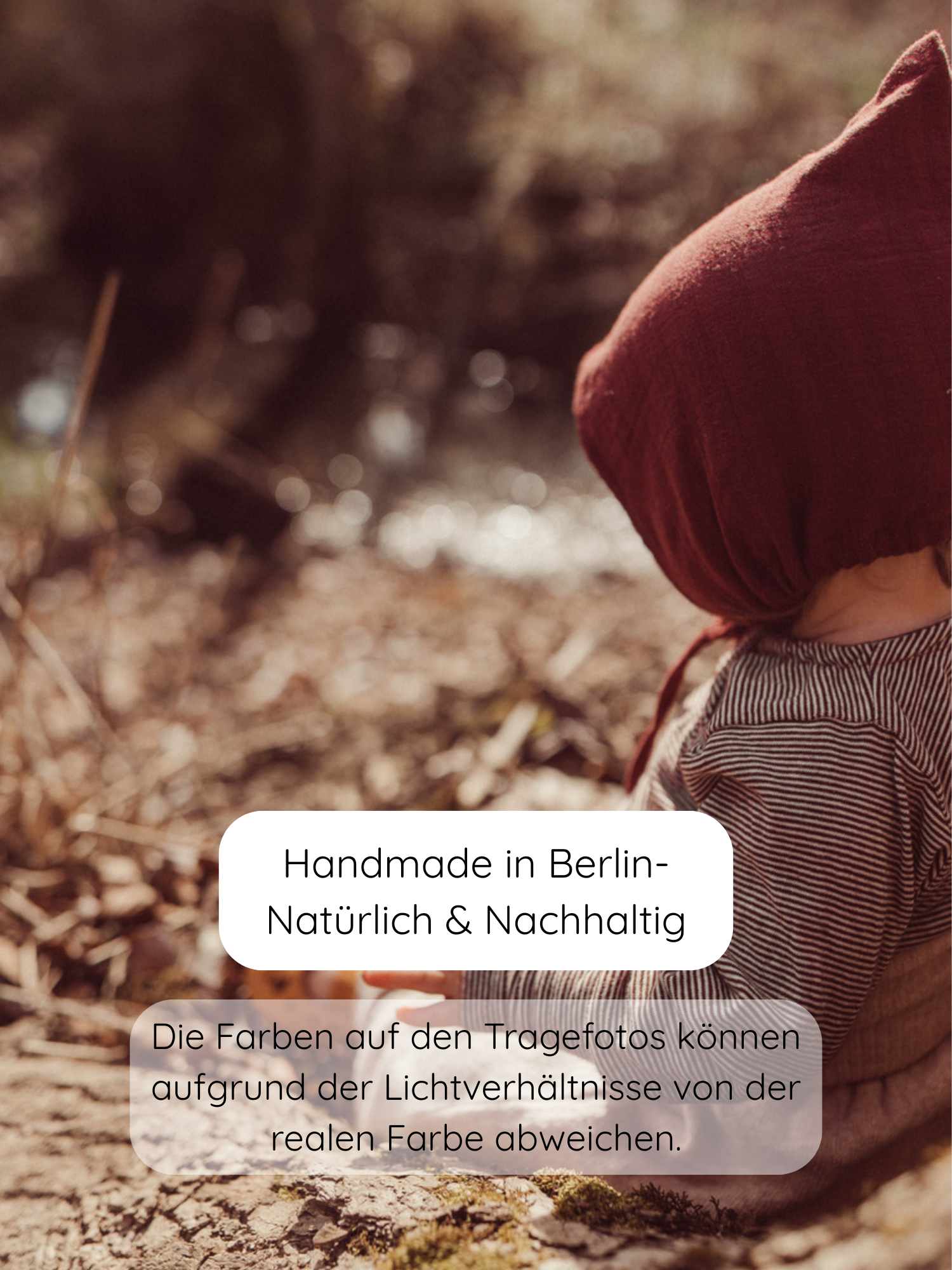 Ein Kleinkind trägt ein rustfarbenes Leinenhäubchen und das Wickelshirt aus Bio-Baumwolle - Ringel Schoko, während es auf dem Waldboden nahe einem Wasser sitzt. Nachhaltig handgefertigt in Berlin.