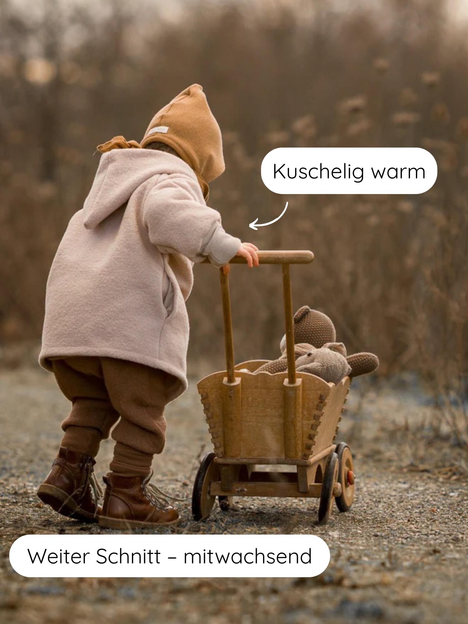 Ein Kleinkind in einer Winter Wichteljacke Wollwalk - Sand schiebt draußen einen Holzwagen mit Strickbär. Die warme Jacke ist aus Bio-Wolle, mit Teddyplüsch gefüttert und mitwachsend.