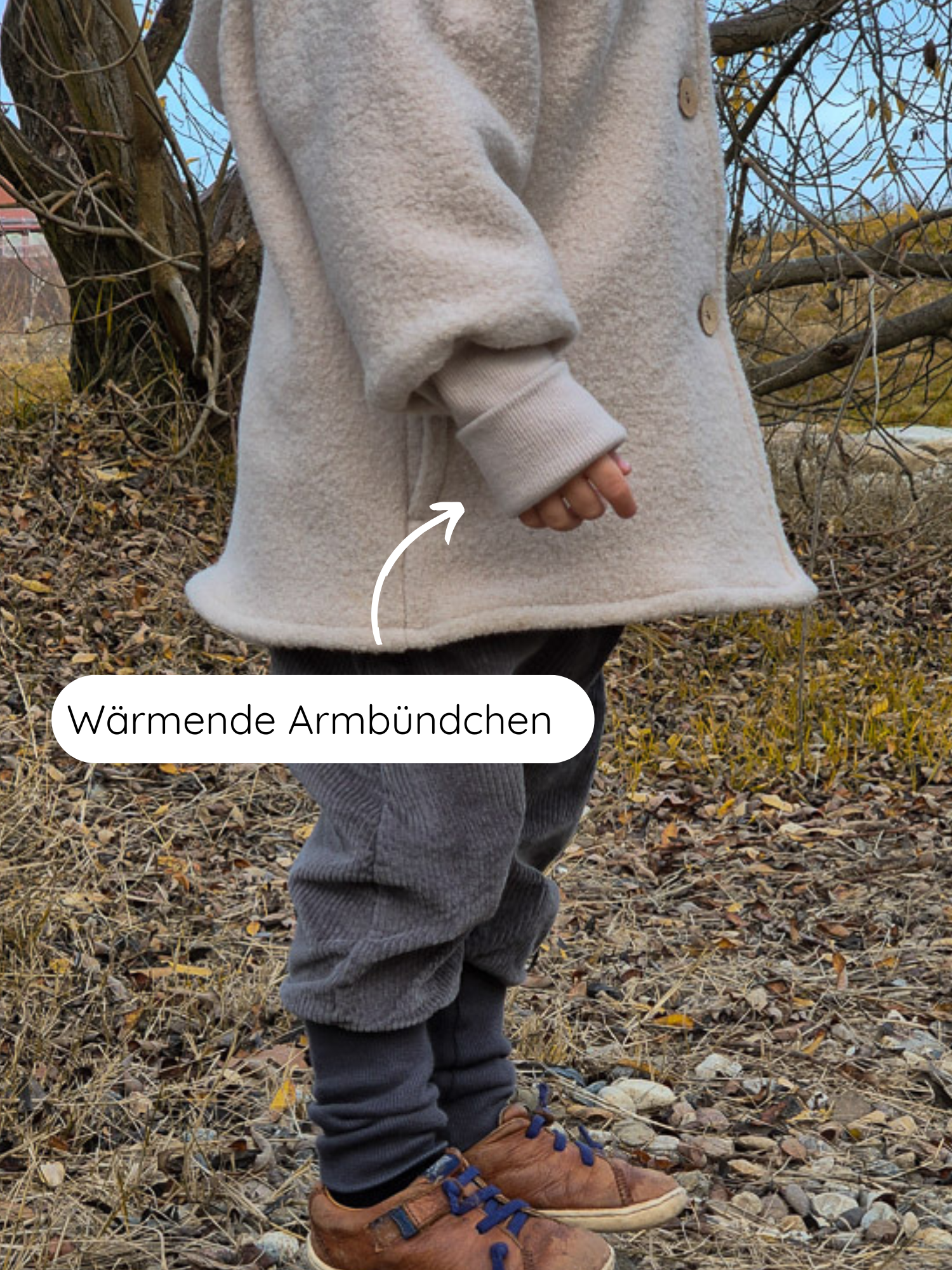Das Bild zeigt ein Kind in der Winter Wichteljacke Wollwalk - Sand mit großen Holzknöpfen, wärmenden Armbündchen und grauer Cordhose, ergänzt durch braune Lederschuhe mit blauen Schnürsenkeln.