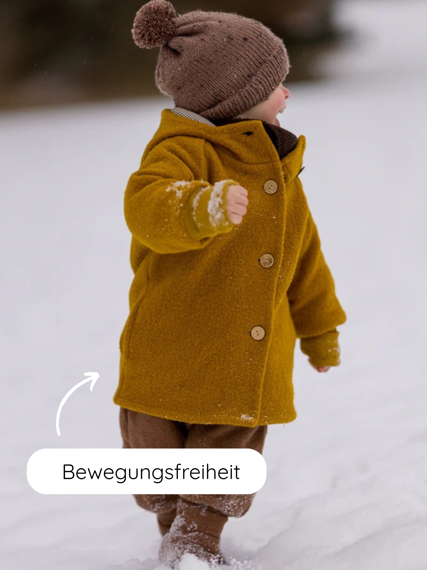 Kleinkind in der Winter Wichteljacke Wollwalk mit Teddyfutter - Honig, läuft im Schnee. Mantel mit Bewegungsfreiheitspfeil, braune Strickmütze, passende Hosen und Fäustlinge, schneebedeckte Stiefel.
