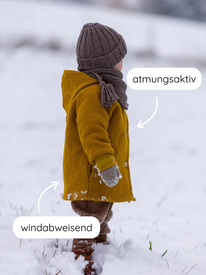 Kleinkind im Schnee trägt die Winter Wichteljacke Wollwalk mit Teddyfutter - Honig. Jacke ist atmungsaktiv und windabweisend, mit spitzer Kapuze und breiten Krempelbündchen.