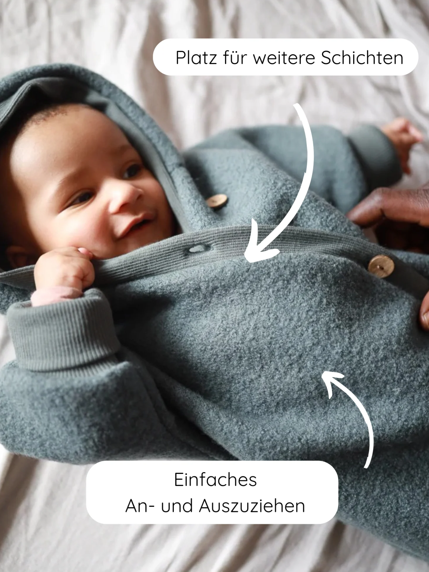 Ein Baby liegt in einem Kuschelanzug Wollwalk - Taube. Zwei Pfeile betonen Platz für weitere Schichten und Einfaches An- und Ausziehen. Hände zeigen das einfache Öffnen des Anzugs.