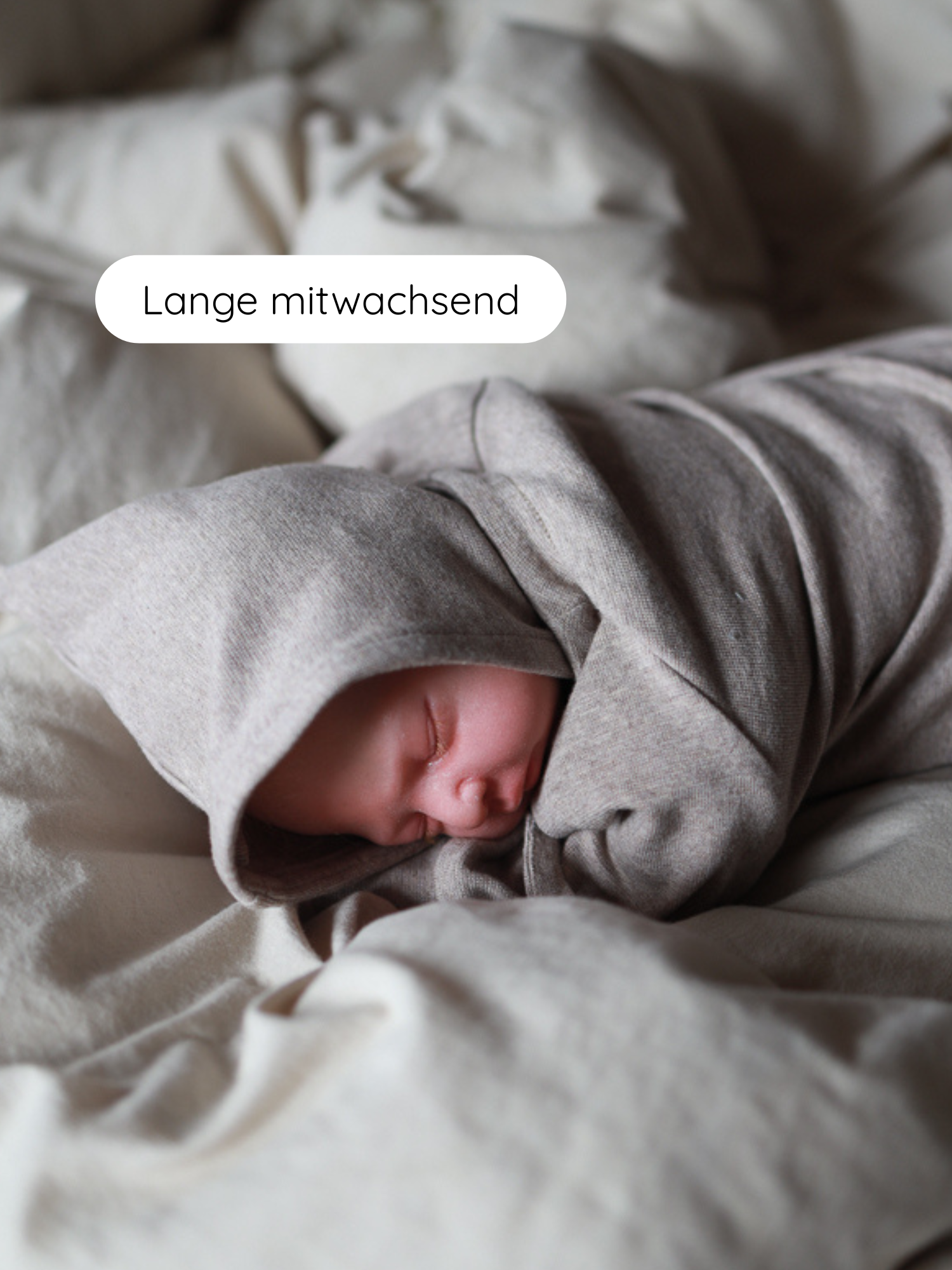 Ein schlafendes Neugeborenes ist in die Zwergenmütze Feinstrick - Hafer Meliert gehüllt, eine weiche, melierte Mütze mit charakteristischem Zipfel, die sanft auf dem Kopf liegt und Ohren wärmt.