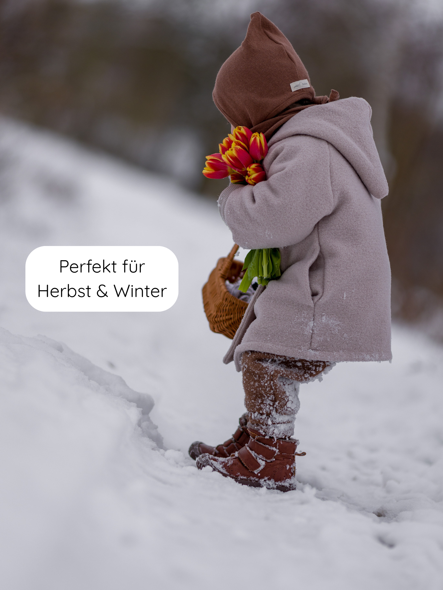 Kleinkind im Schnee mit Zwergenmütze Strick - Nougat aus recycelter Baumwolle, trägt warme Herbst-/Winterkleidung. Mütze passt perfekt, hält warm und ist mit Bindeband verstellbar.