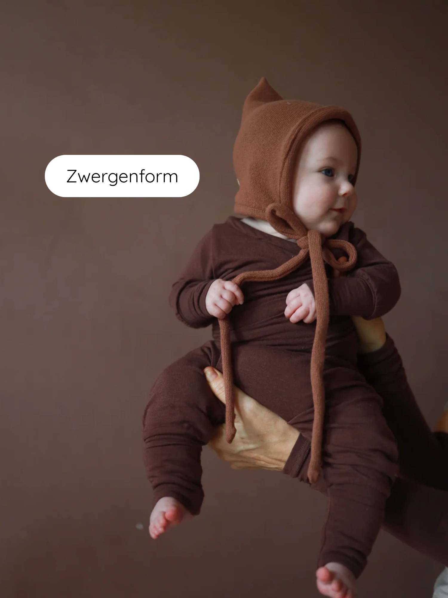 Baby in Schokobraunem Strickanzug mit spitzer Zwergenmütze Strick - Nougat aus recycelter Baumwolle, gehalten von Erwachsenen; Mütze mit Bindeband für perfekte Passform, ideal für Herbst und Winter.