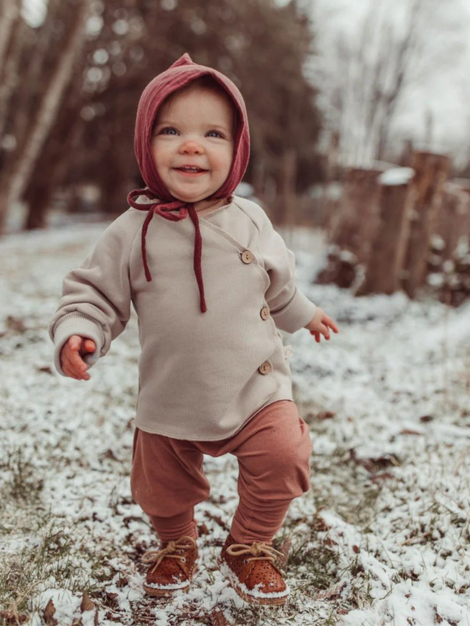 Kleinkind trägt Babyknicker Kaschmir-Mix - Zimt, erkundet schneebedeckten Weg. Hose mit Klappbündchen, ideal für Neugeborene, bietet Wärme und Komfort bei ersten Schritten.