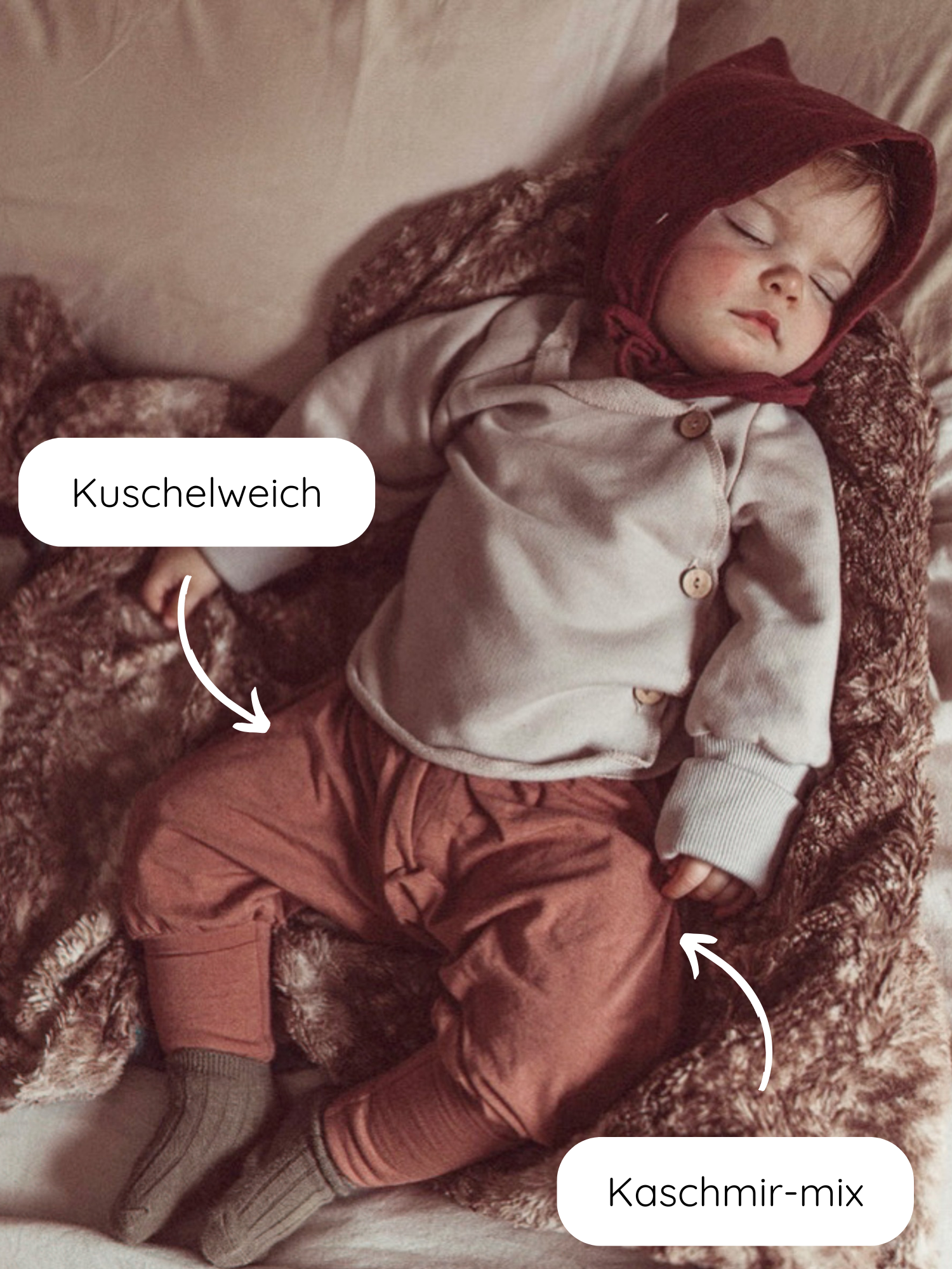 Babyknicker Kaschmir-Mix - Zimt: Ein Baby schläft auf einer weichen Decke, trägt kuschelweiche Kaschmir-Mix-Kleidung in Erdtönen mit umklappbaren Bündchen, ideal für Komfort und Wärme.