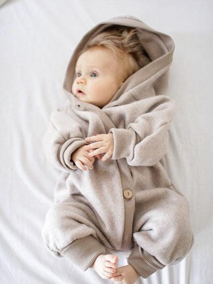 Baby in einem beigen petit cochon Kuschelanzug aus Bio-Baumwollfleece mit Wichtelkapuze und schräger Knopfleiste