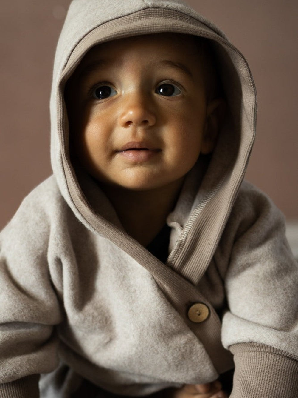 Baby in einem petit cochon Overall aus beigem Bio-Baumwollfleece mit Wichtelkapuze und schräger Knopfleiste