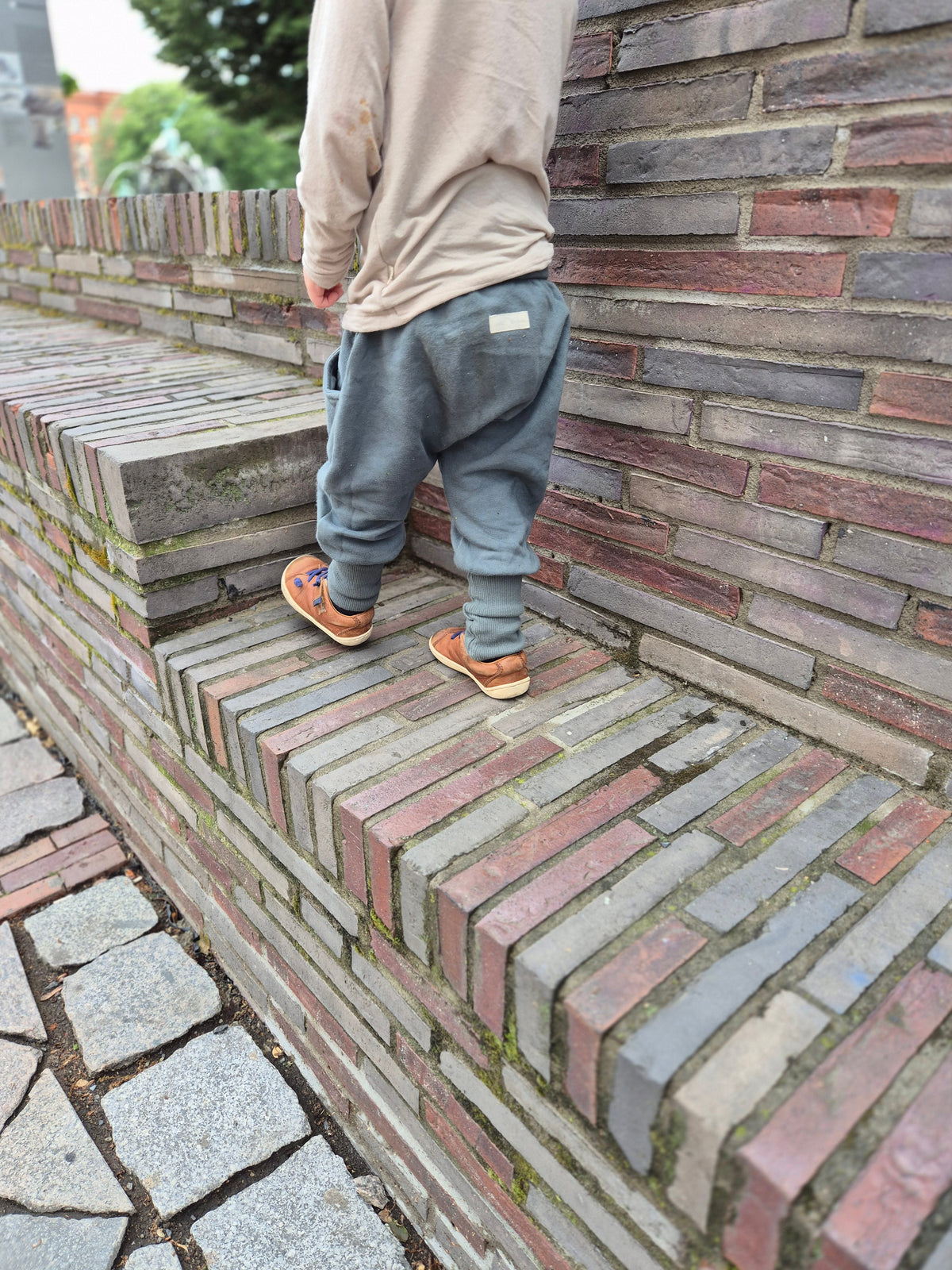 Kind trägt eine bequeme petit cochon Knickerbocker Hose aus Bio-Sweat in Schoko beim Treppensteigen im Freien.