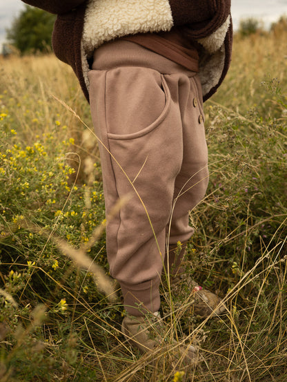 petit cochon Knickerbocker Hose aus schokobraunem Bio-Sweat mit elastischen Bündchen und Kokosknöpfen auf einer Wiese