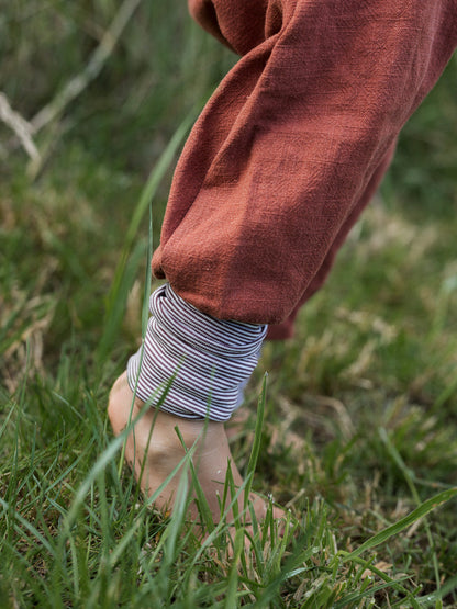 petit cochon Knickerbocker aus rostrotem Leinen mit gestreiftem Bündchen für Kinder beim Spielen im Gras