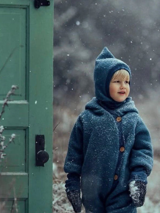 petit cochon Schlupfmütze aus blauem Wollwalk mit Bio-Jersey Futter an einem Kind im Schnee
