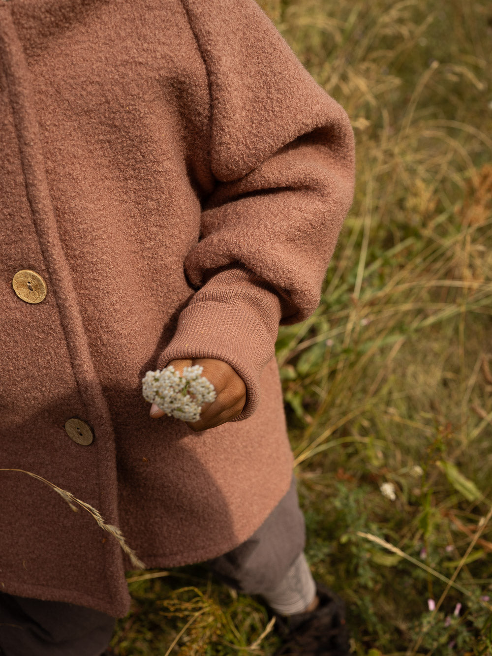 petit cochon Wichteljacke aus altrosa Wollwalk mit Bio-Jersey-Bündchen und Holzknöpfen bei einem Kind im Freien
