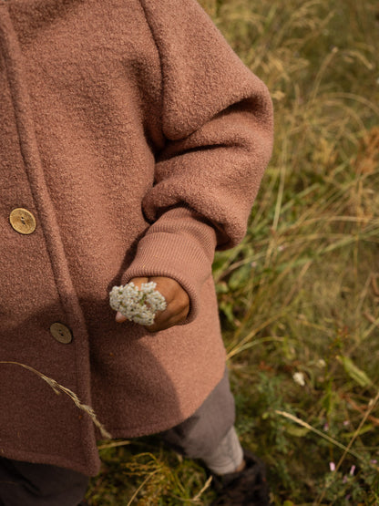 petit cochon Wichteljacke aus altrosa Wollwalk mit Bio-Jersey-Bündchen und Holzknöpfen bei einem Kind im Freien
