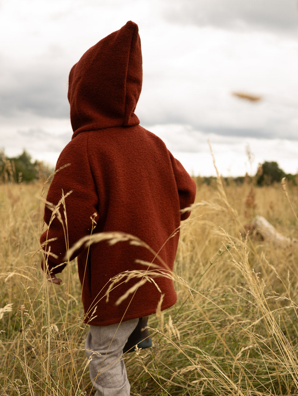 Kind in rostroter petit cochon Wollwalk-Wichteljacke mit Kapuze beim Spielen auf einem herbstlichen Feld