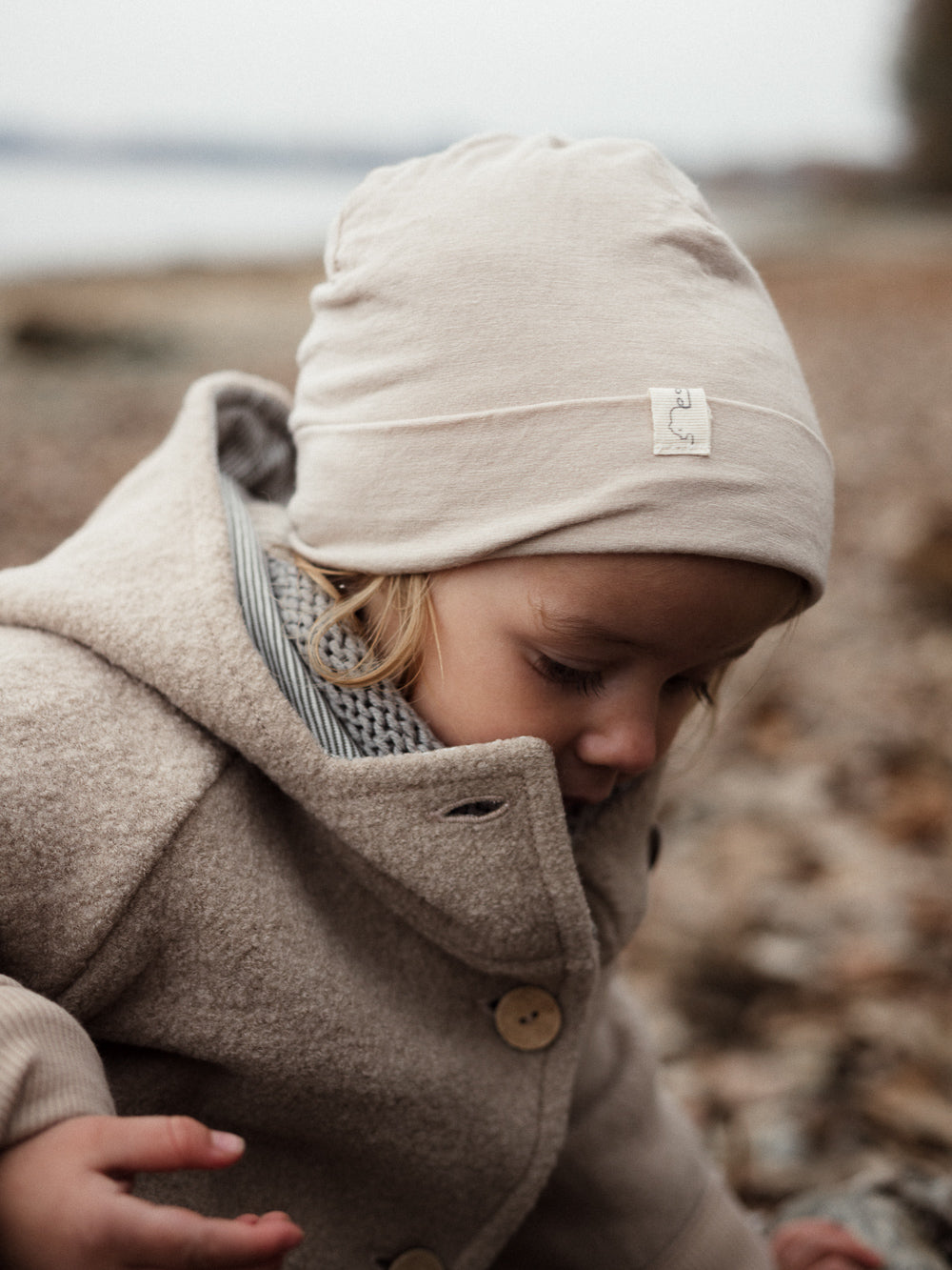 Kind in beiger petit cochon Wollwalk-Wichteljacke mit Kapuze und Bio-Jersey-Futter beim Spielen im Freien