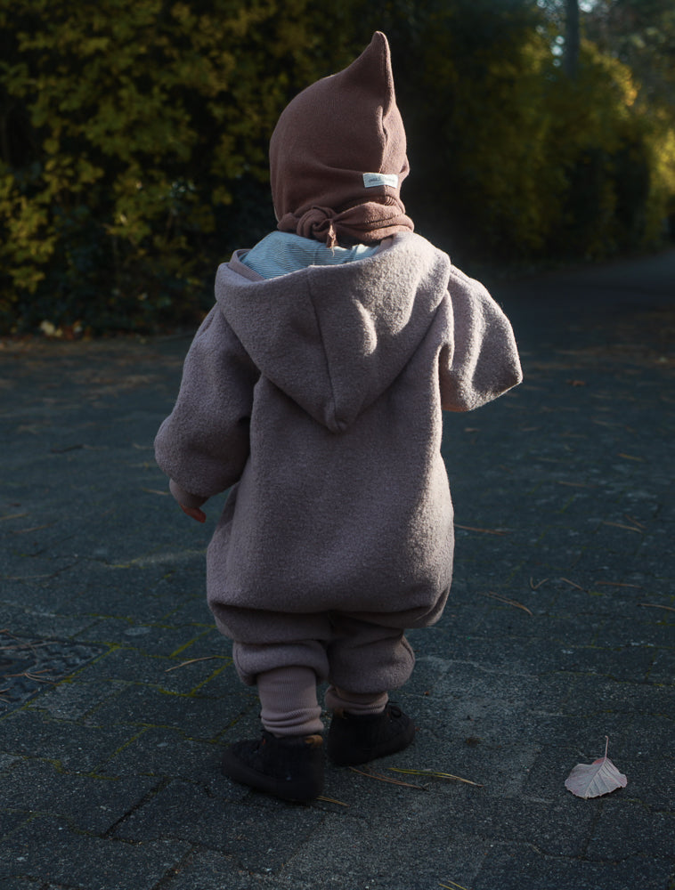 Kleinkind von hinten im Kuschelanzug Wollwalk - Puder, bestehend aus einem weichen, kapuzenlosen Mantel mit passenden Hosen, ideal für Herbstspaziergänge. Der Anzug ermöglicht Bewegungsfreiheit und Wärmeschutz.