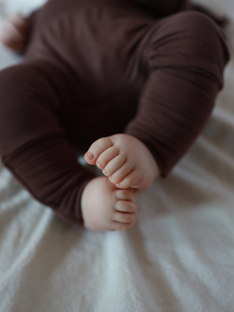 Babyknicker Bambusviskose Zartbitter: Chubby Babybeine in weichen, atmungsaktiven braunen Leggings aus Bambusviskose, bequem auf einer hellen Unterlage ruhend, bieten Bewegungsfreiheit und sanften Tragekomfort.