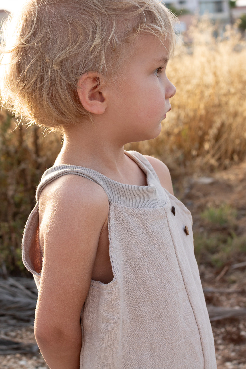 Ein Kleinkind trägt eine Schlupflatzhose Leinen - Sand aus 100% Leinen, mit lockerer Passform und ribbbedem Ausschnitt, perfekt für Bewegungsfreiheit und Komfort im Freien an warmen Tagen.