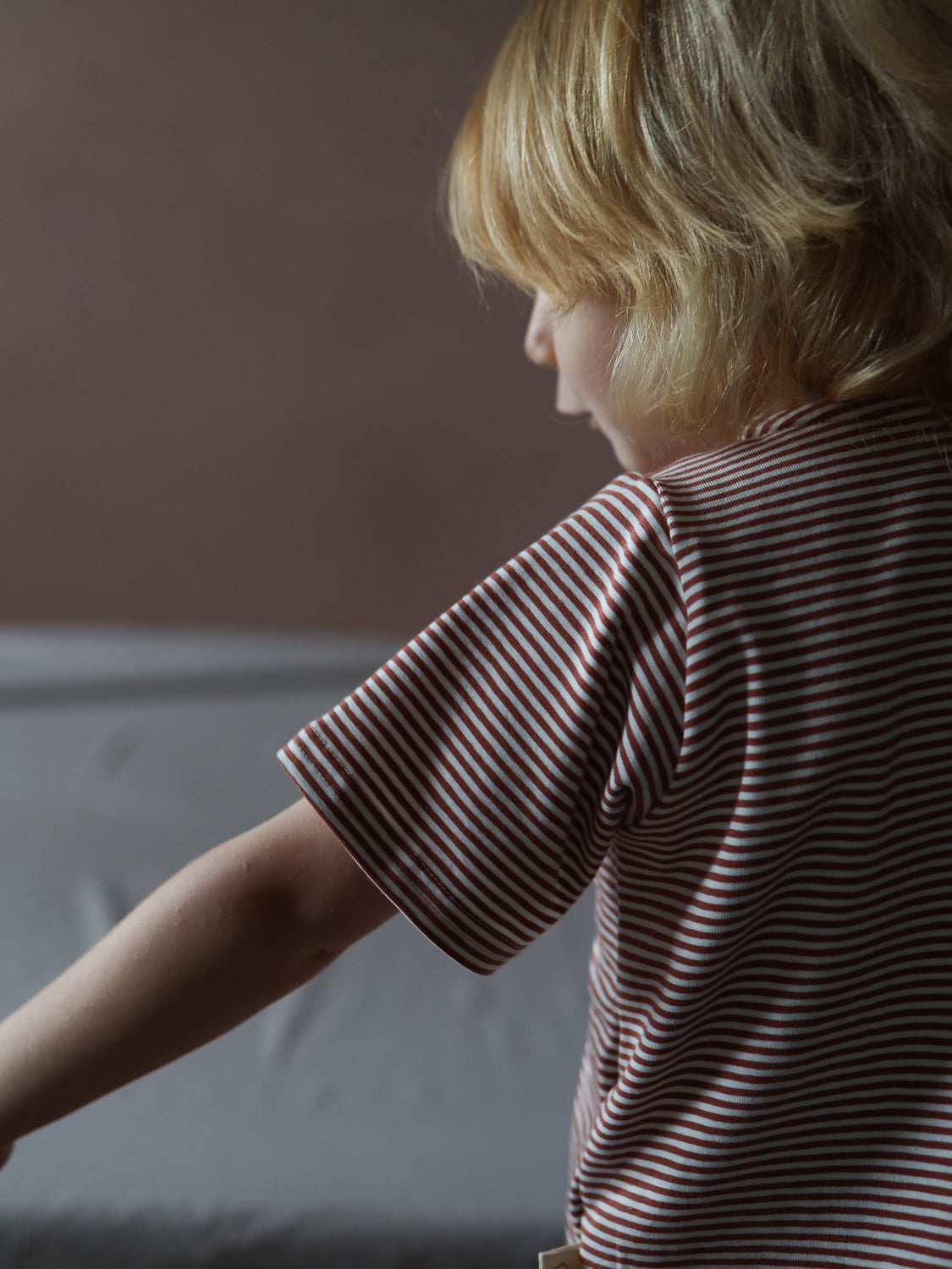 Ein Kind trägt das Kurzes Wickelshirt Baumwolle - Ringel Ziegel mit schmalen roten und weißen Streifen. Das kurzärmelige Design ist angenehm weich und ideal für den Sommer.