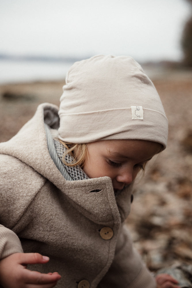 Ein Kleinkind trägt die Wichteljacke Wollwalk - Sand. Die beige Wolljacke aus hochwertigem Wollwalk mit großen Knöpfen bietet Bewegungsfreiheit und Wärme, ideal für Herbst- und Winterabenteuer.