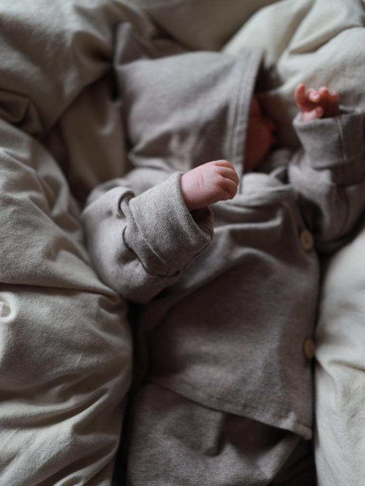 Neugeborenes in taupefarbenem Zwergenmütze Feinstrick - Hafer Meliert, zeigt weichen Jersey-Stoff und klassische Zwergenform mit kleinem Zipfel. Kuscheliges, warmes Design, perfekt für empfindliche Babyhaut.