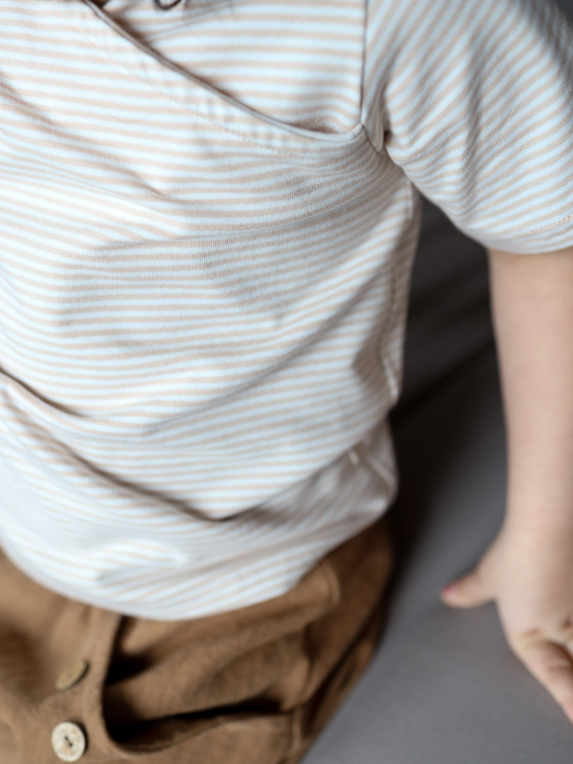 Nahaufnahme eines Kurzes Wickelshirt Baumwolle - Ringel Sand. Das gestreifte Shirt ist in eine braune Hose gesteckt. Der rechte Arm des Trägers ist sichtbar, das Shirt wirkt leicht und bequem.
