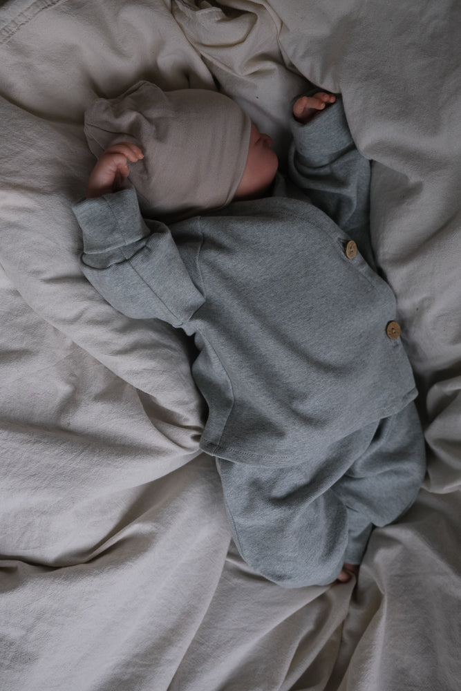 Neugeborenes in grauem Strick-Set mit Holzknöpfen, trägt Babyknicker Feinstrick - Mint Meliert. Weiches, atmungsaktives Material, ideal für Bewegungsfreiheit. Perfekt für den Alltag. Nachhaltig in Berlin gefertigt.