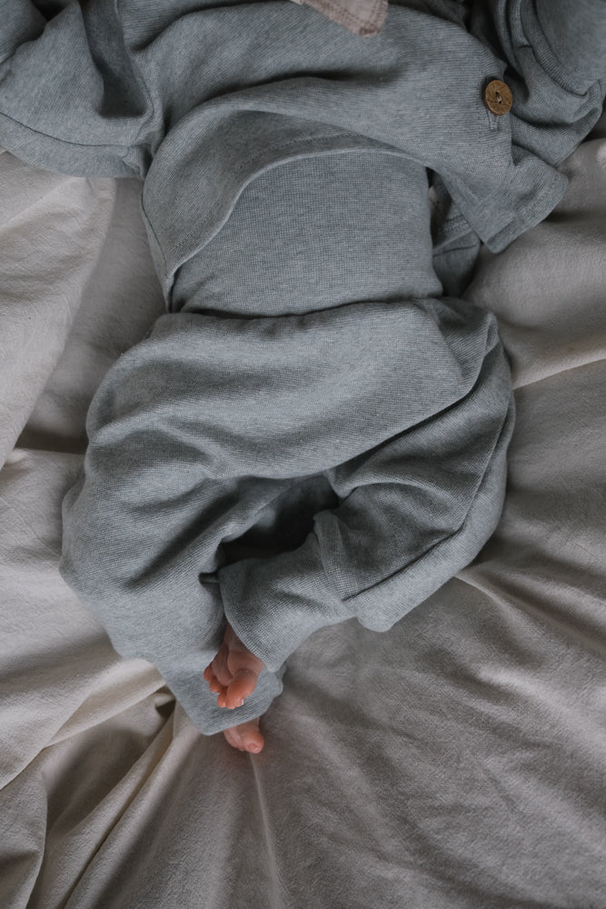 Ein Baby liegt auf hellem Untergrund, gekleidet in den Babyknicker Feinstrick - Mint Meliert, die weiche, atmungsaktive Hose bietet Bewegungsfreiheit, ideal für Alltag und Kita.