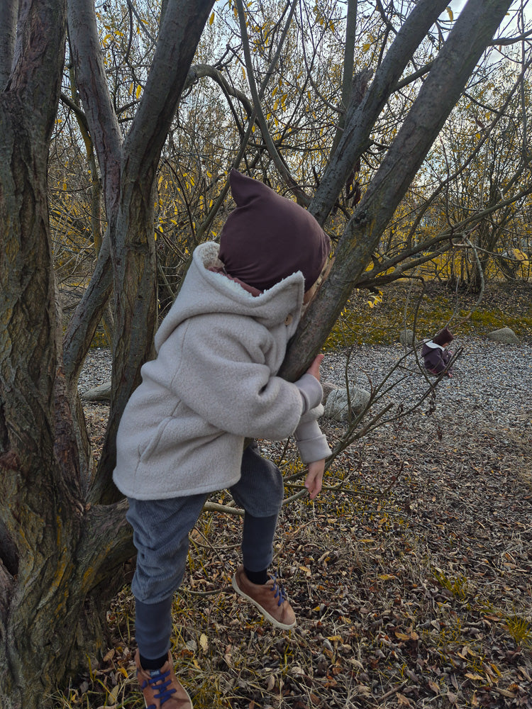 Kind klettert auf Baum in Knickerbocker Breitcord Stretch - Maus, ideal für Übergangszeit. Die bequeme Hose bietet Bewegungsfreiheit und Komfort, perfekt für kleine Entdecker:innen bei kühlerem Wetter.